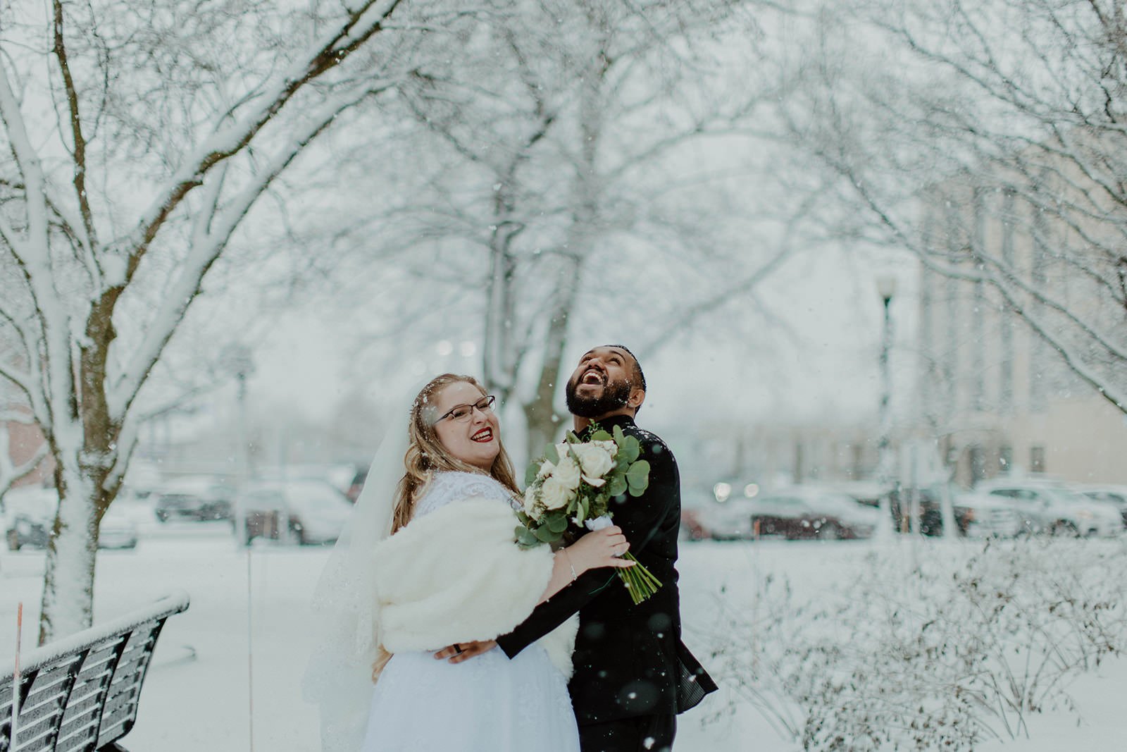 Bride and groom hug while laughing in the snow