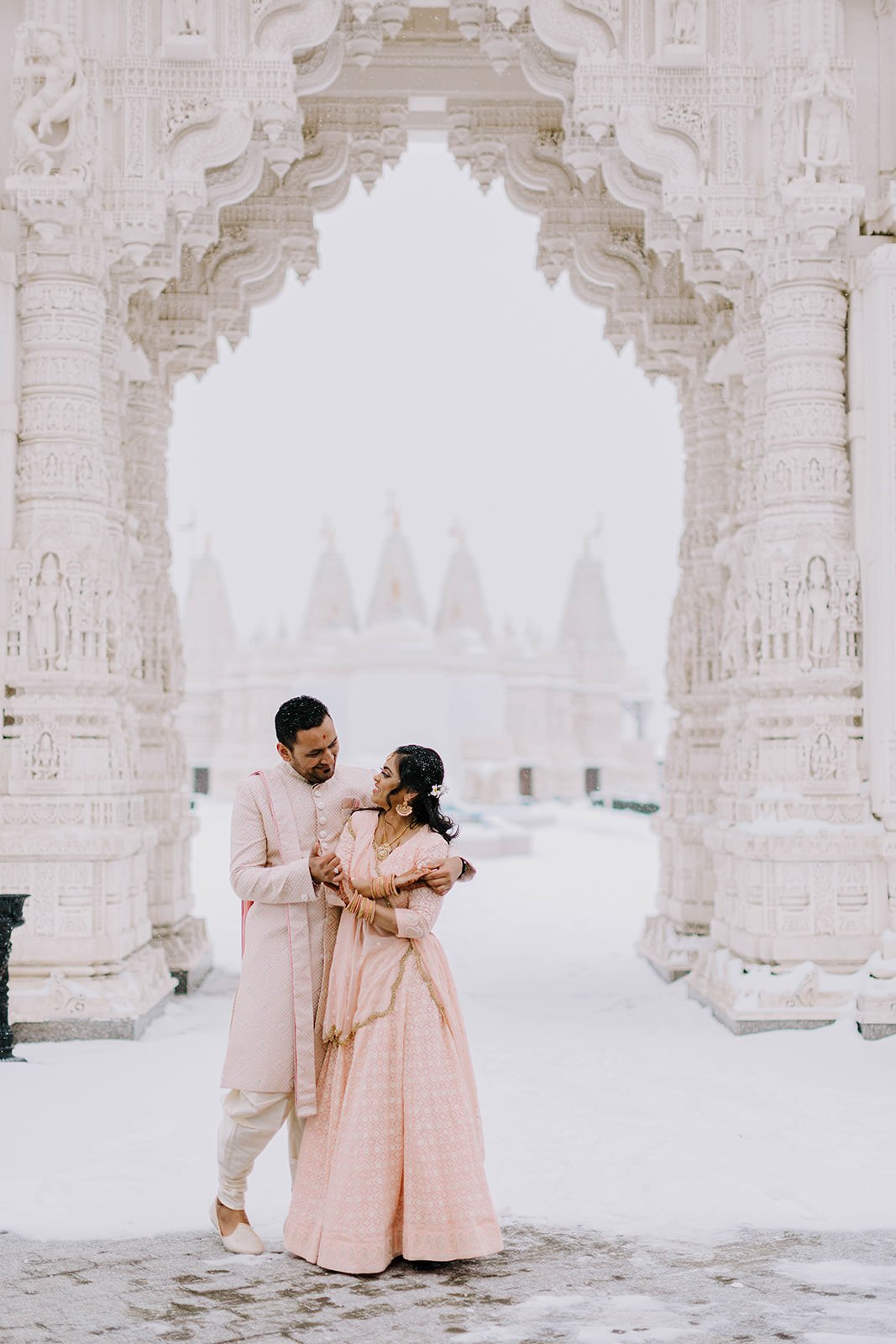 Newlywed couple embrace in front of snow covered  Hindu temple