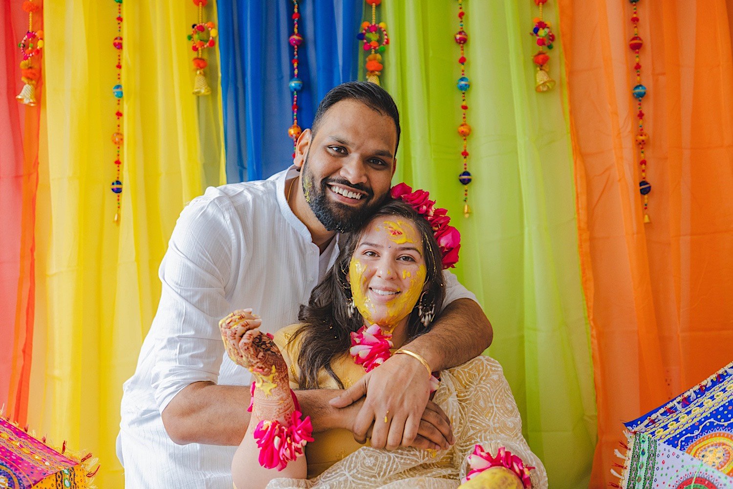 Man hugs his fiancee from behind while she's covered in turmeric during traditional Haldi celebration