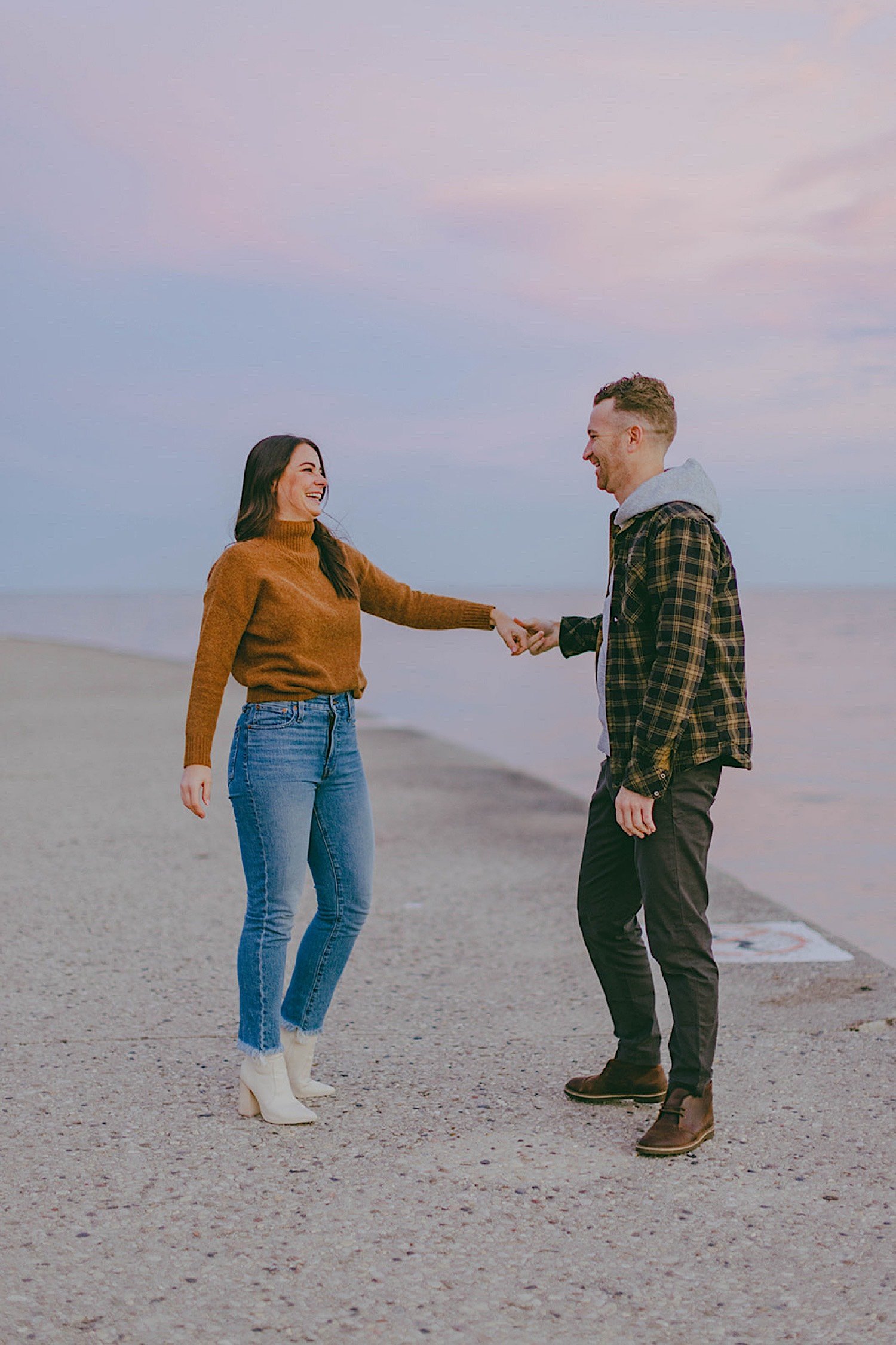 Couple hold hands and laugh in front of Lake Michigan during blue hour