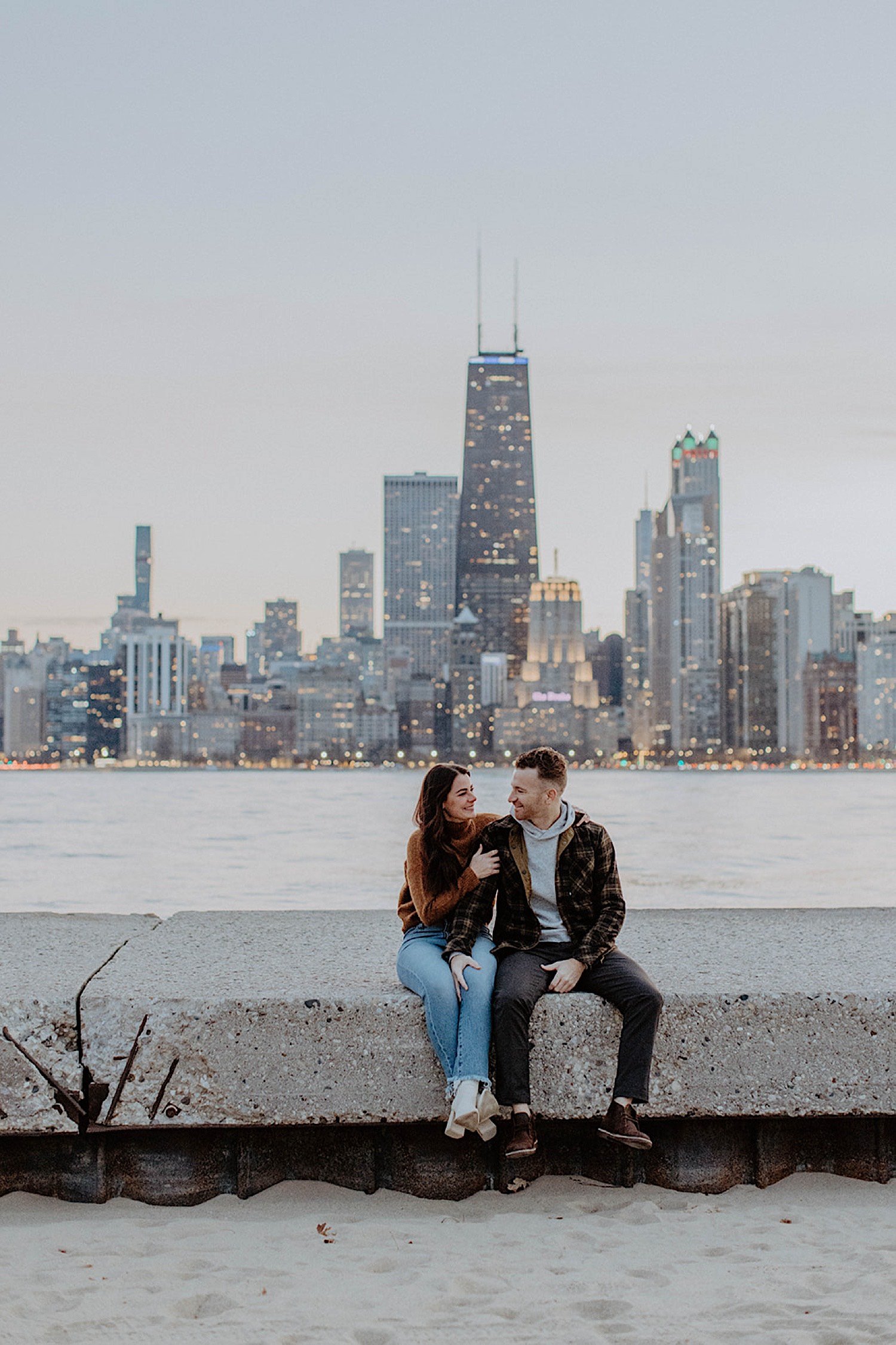 Couple sit next to each other after their North Avenue Beach engagement with the Chicago skyline behind them