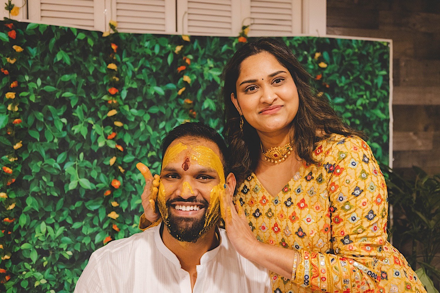 Bride covers grooms face in turmeric during traditional Haldi celebration as they smile at the camera