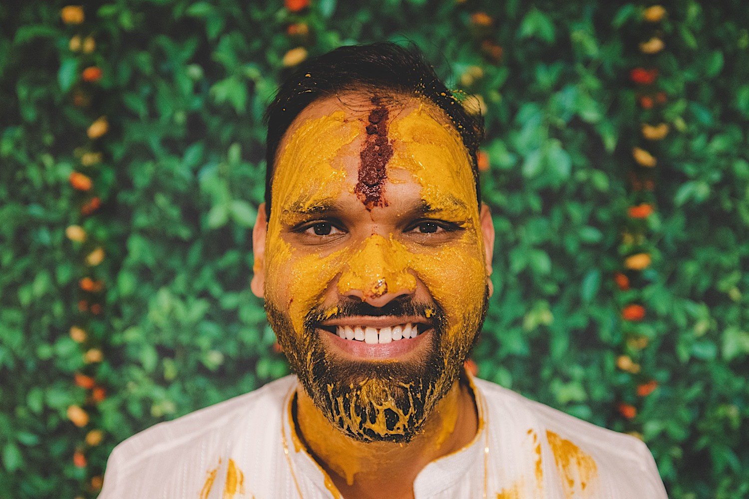 Groom smiles at camera covered in turmeric at traditional Haldi celebration