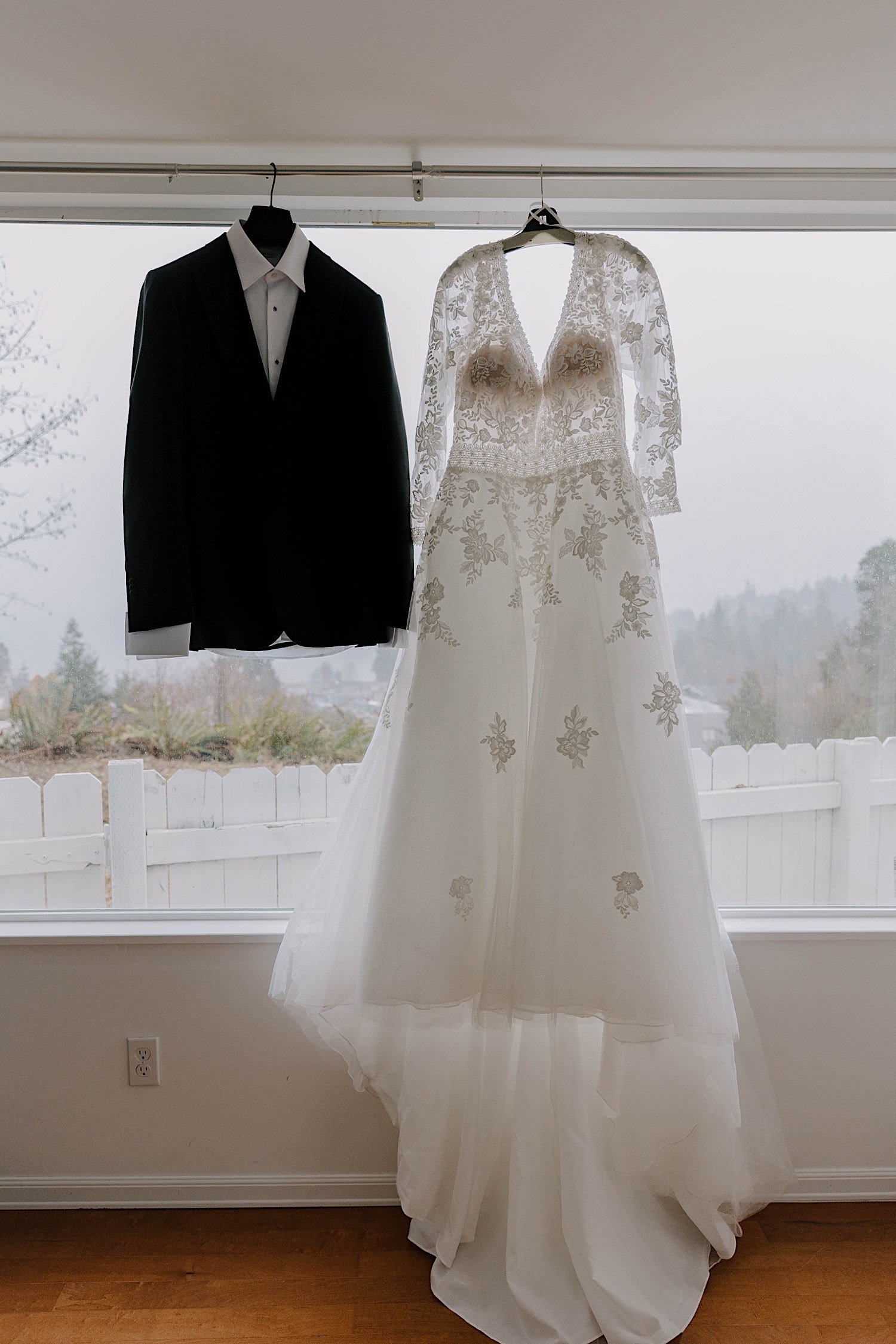 Hanging wedding dress and suit in front of a window