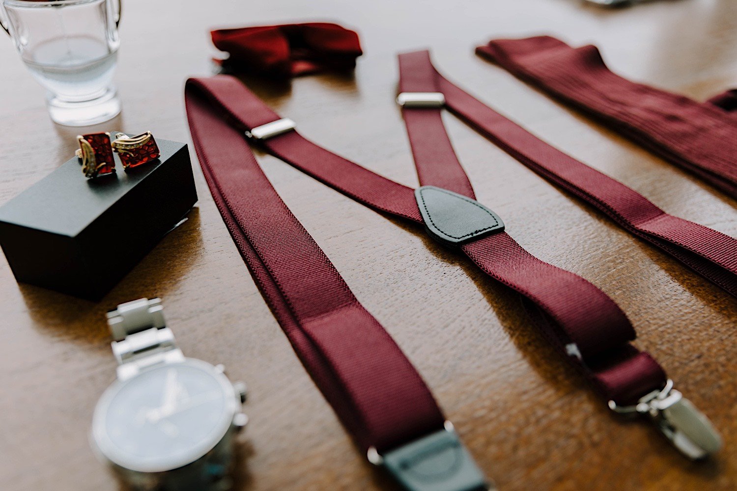 Photo of a watch, rings, and straps laid out on a table prior to a wedding