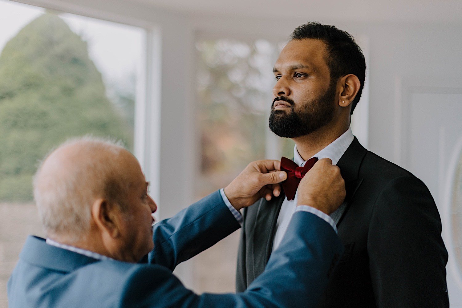 Father adjusts son's bowtie as they get ready for the son's wedding