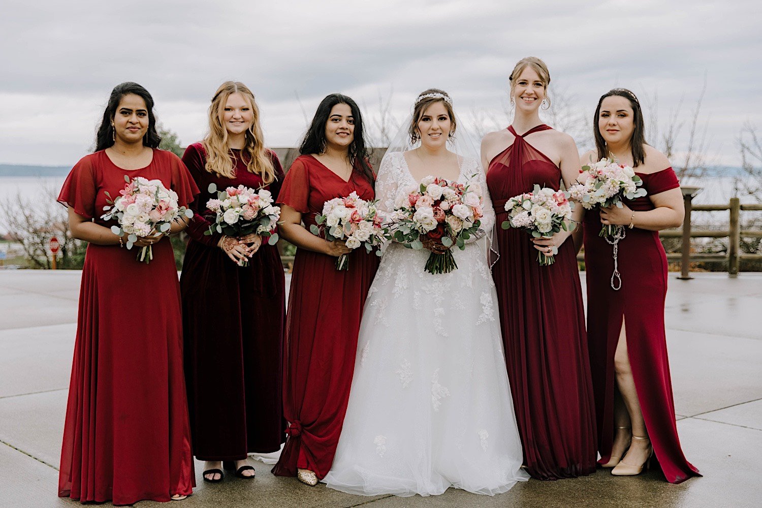 Bride and bridesmaids pose together and smile at the camera outside the Rosehill Community Center