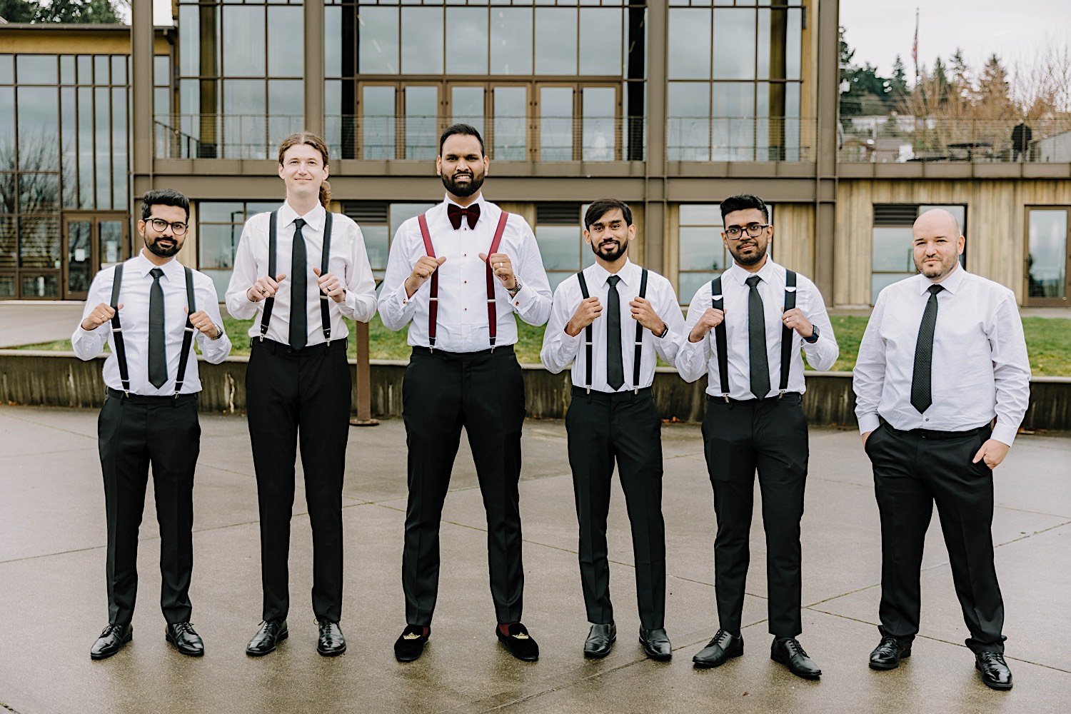 Groom and groomsmen pose together looking at the camera outside the Rosehill Community Center