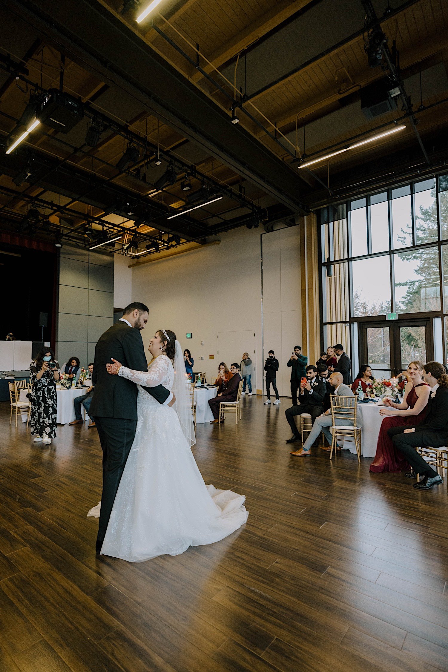 Bride and groom share their first dance together as their wedding guests watch inside the Rosehill Community Center