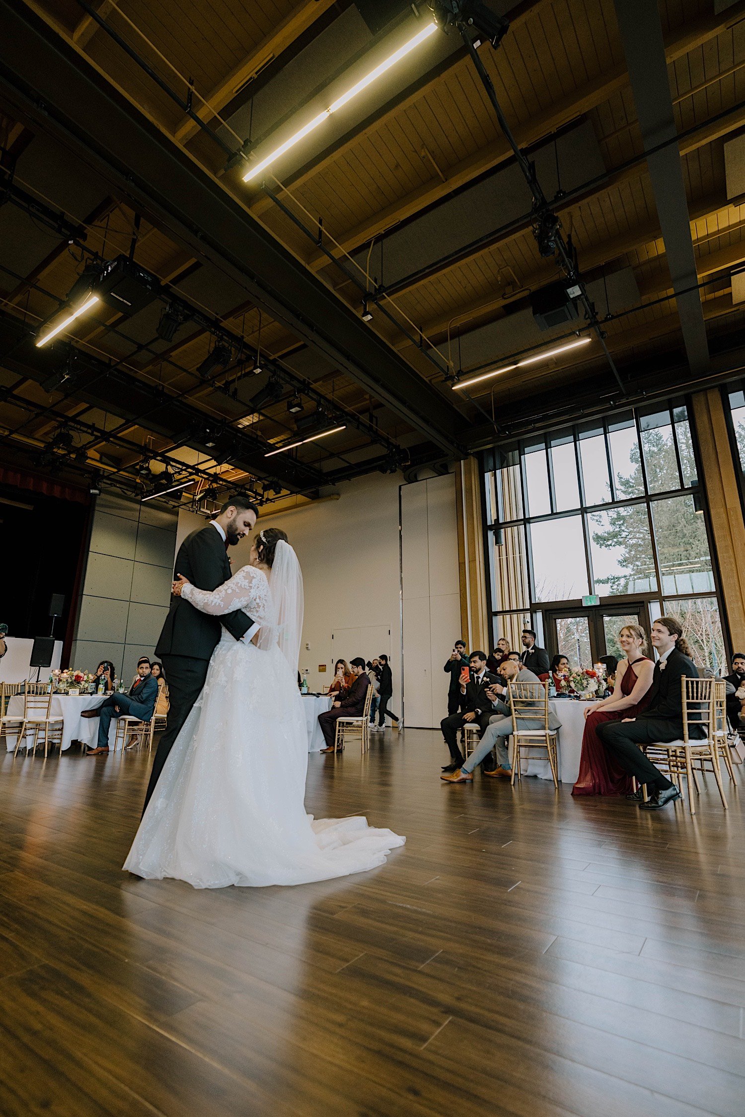 Bride and groom share their first dance together as their wedding guests watch inside the Rosehill Community Center
