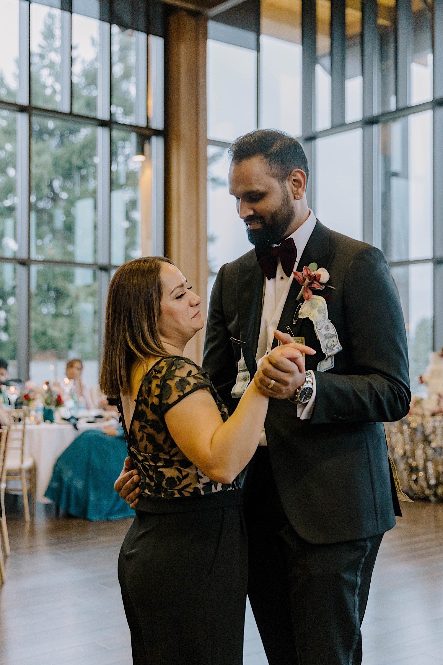 Groom and mother share a dance together as wedding guests sit in the background