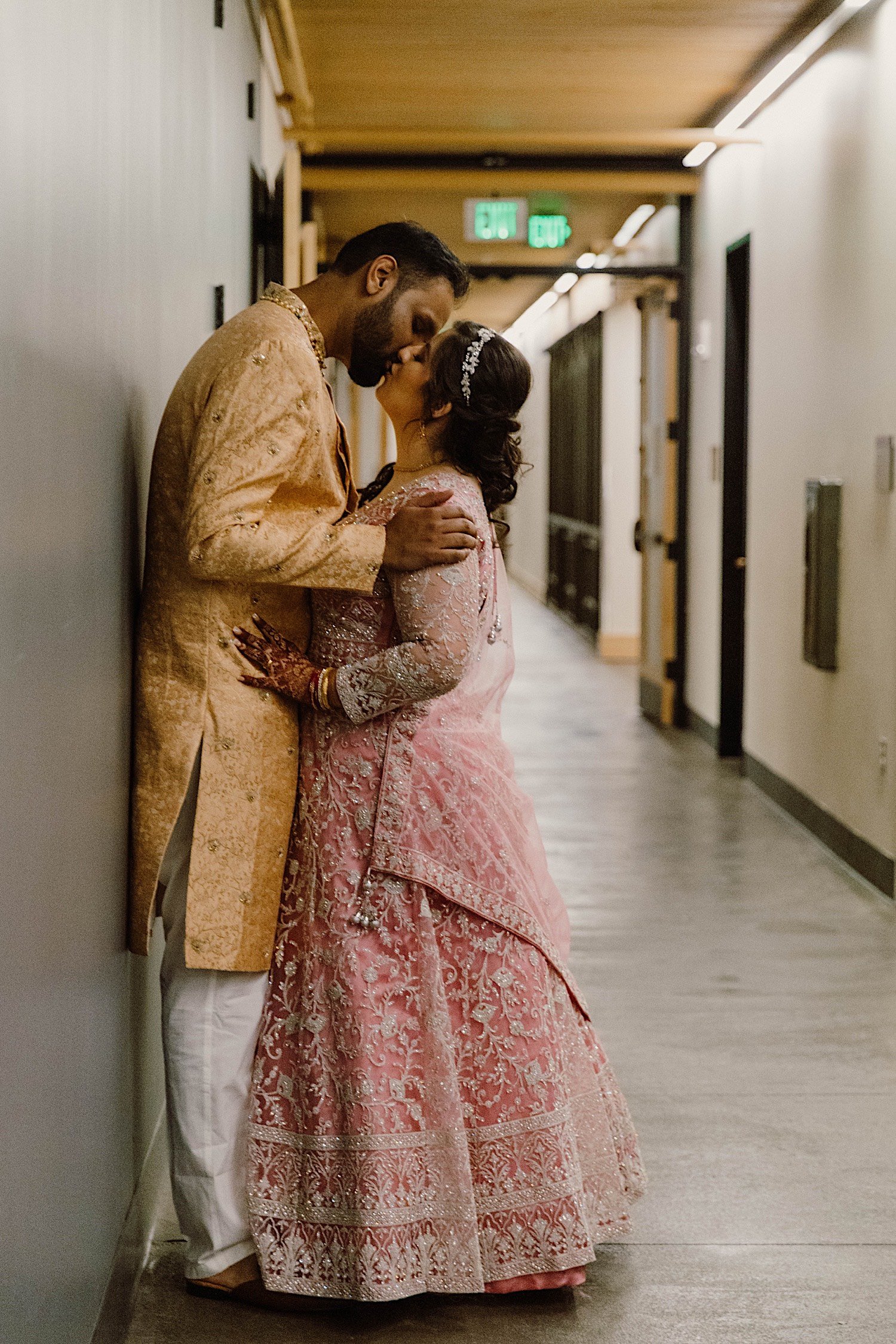 Bride and groom kiss in hallway of venue away from everyone