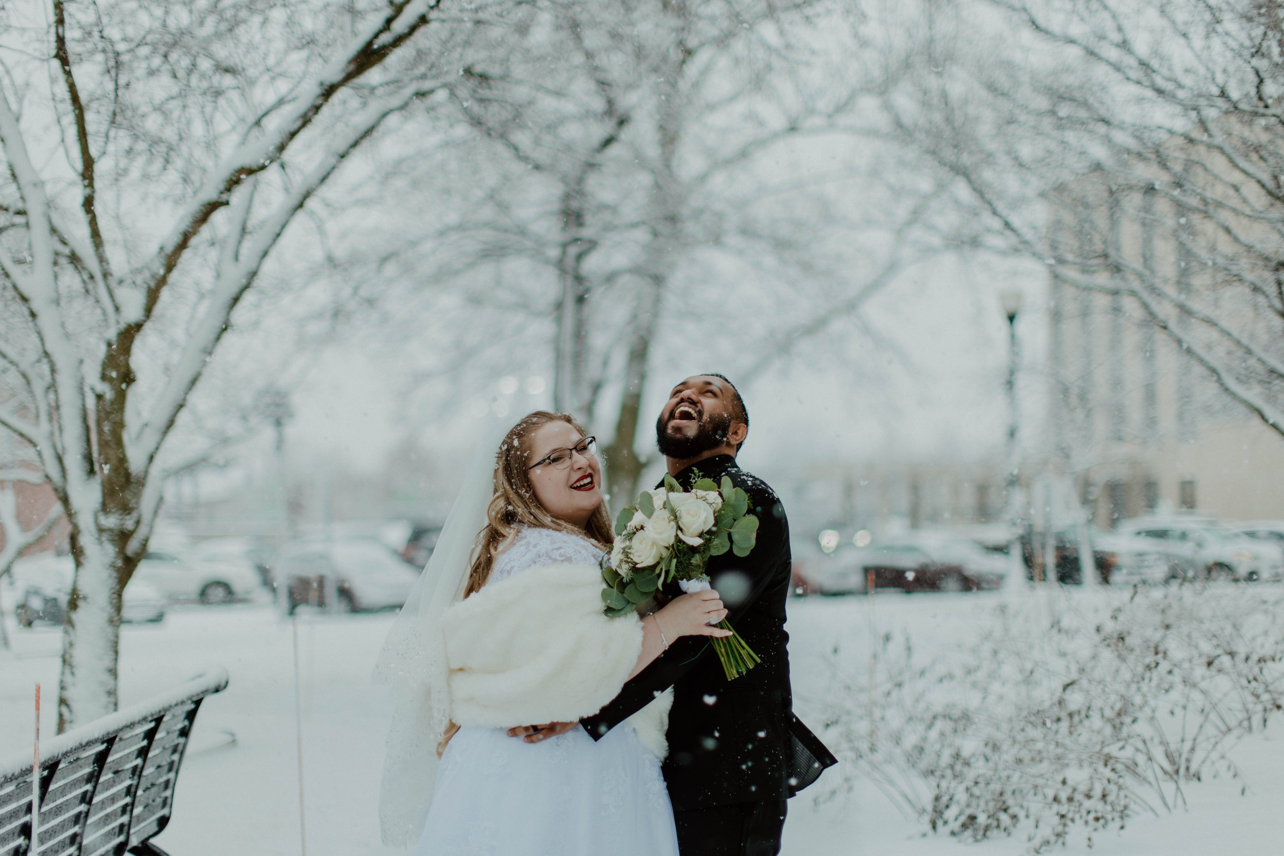 Newlyweds hold each other and laugh with snow falling around them