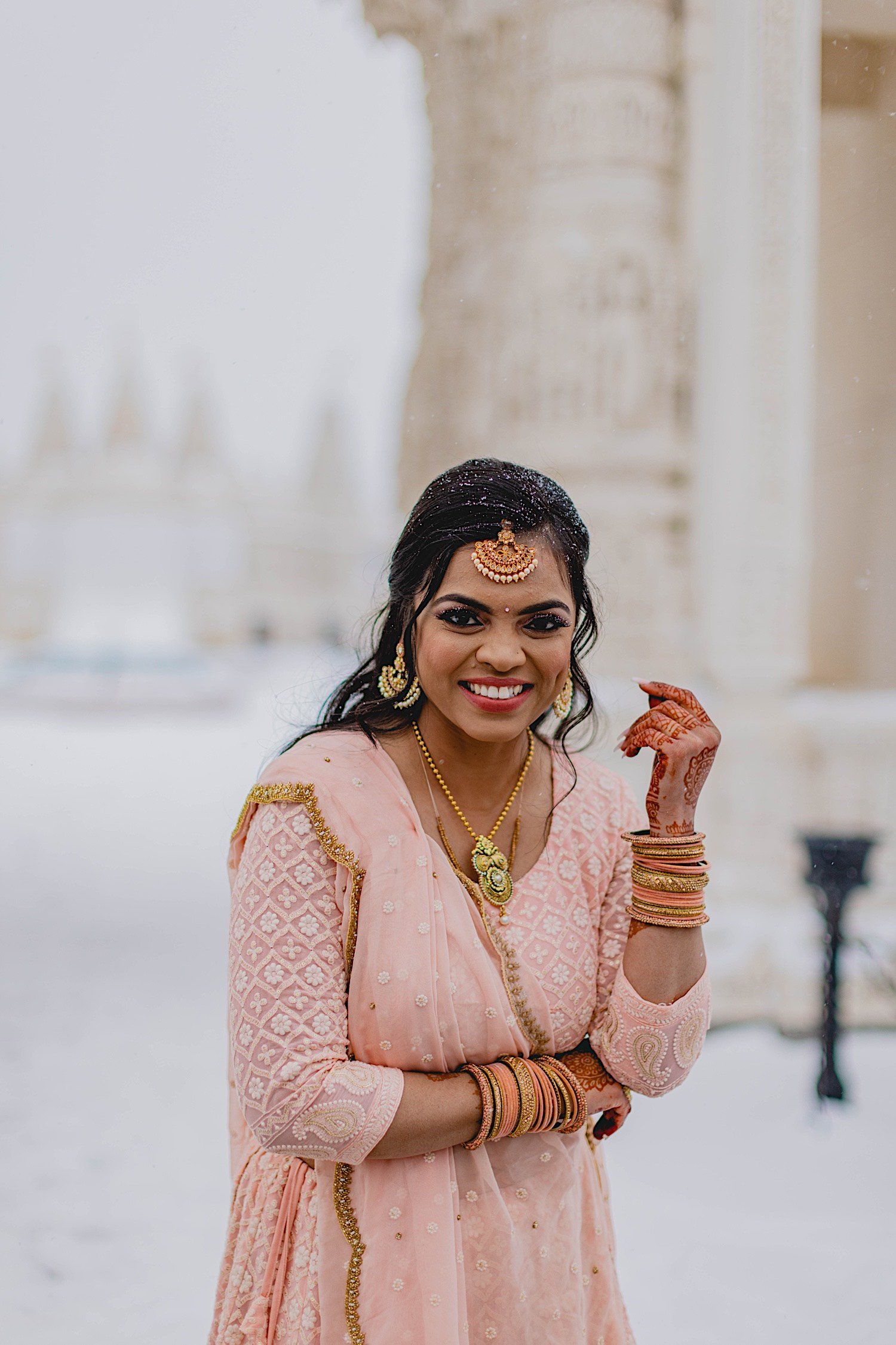 Bride wearing traditional Indian wedding attire smiles at the camera with snow in the background