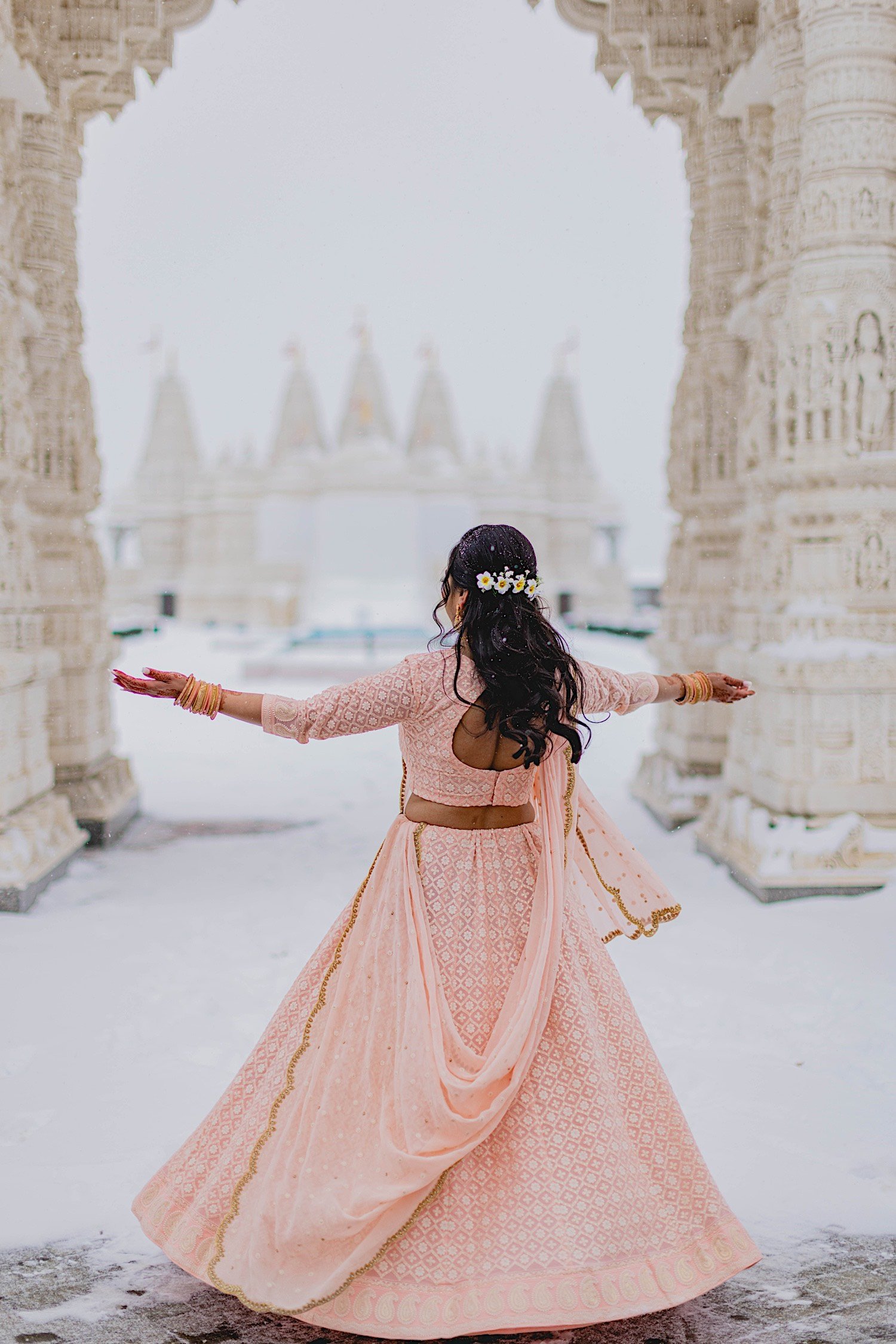 Bride wearing traditional Indian wedding dress dances in the snow