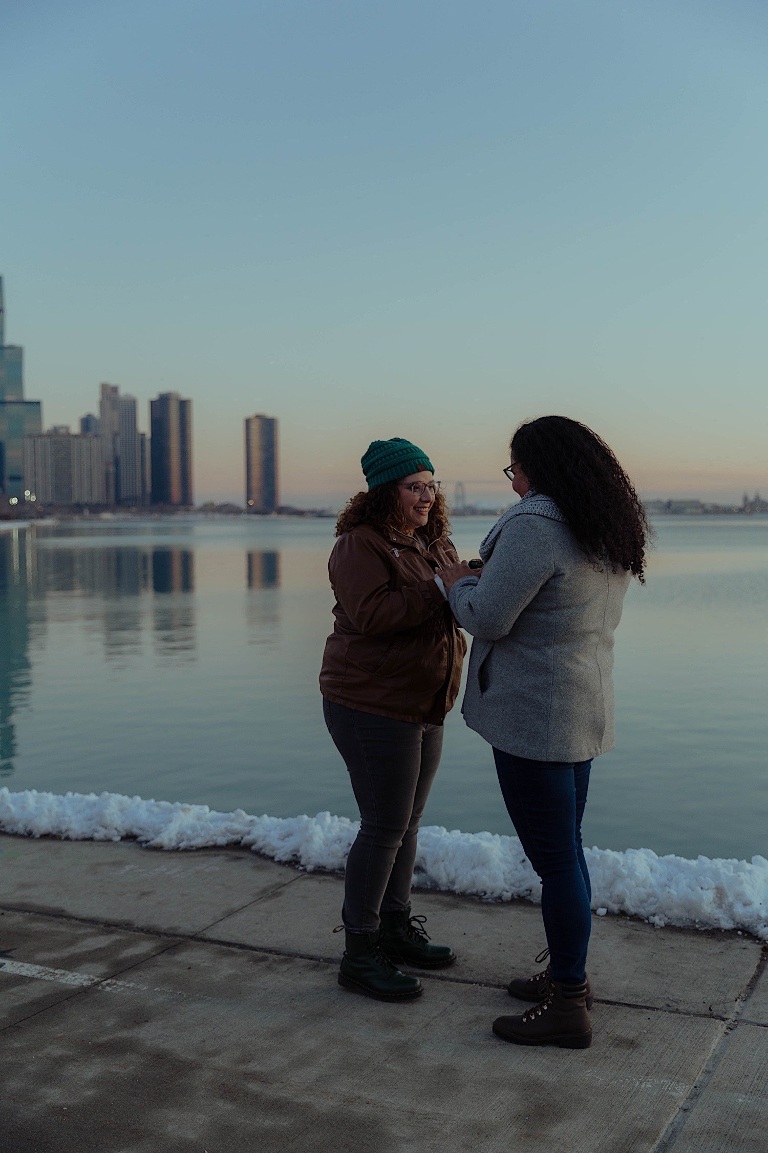 Couple standing with one another putting their engagement ring on in front of a snowy Lake Michigan