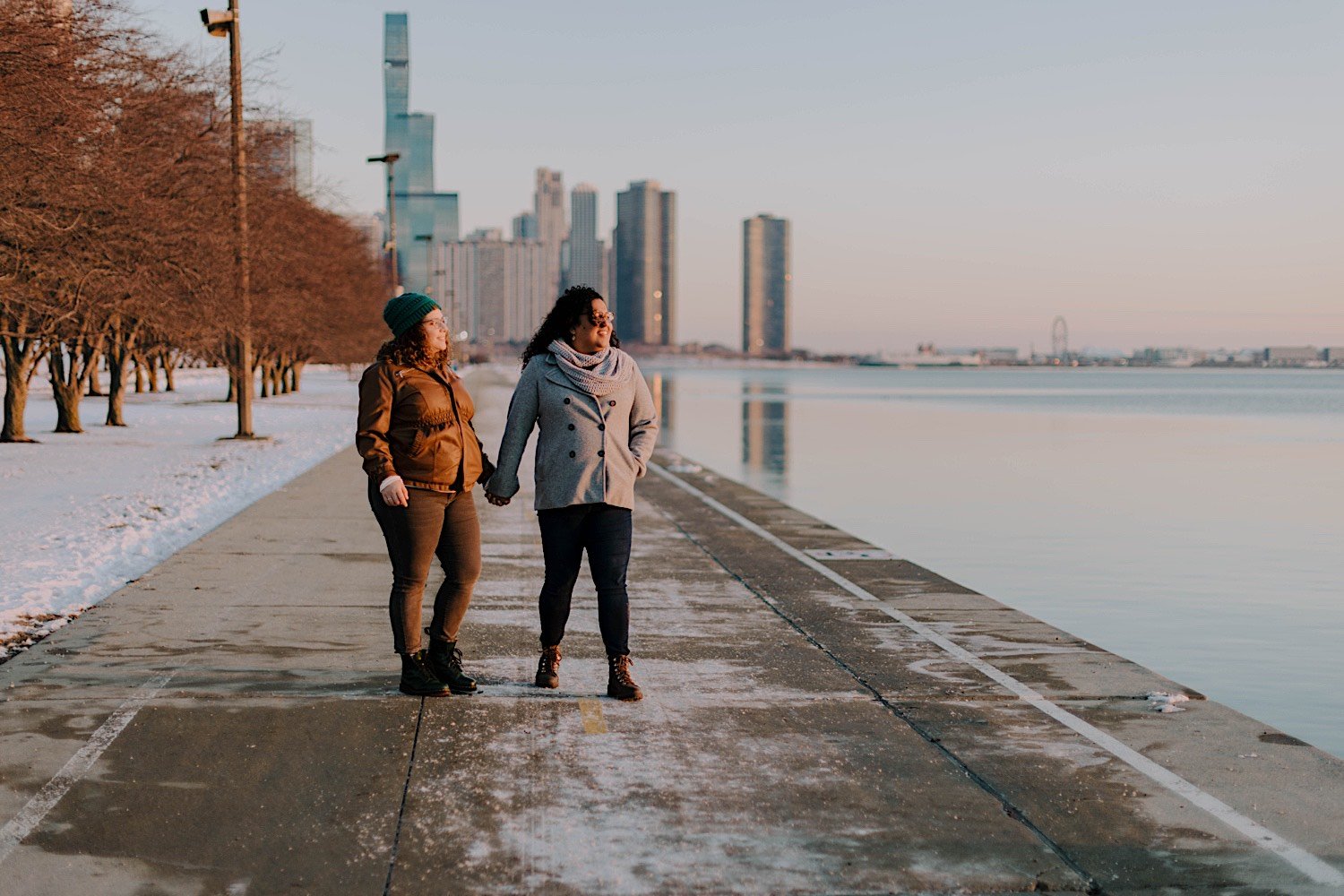 Couple stand and hold hands with the Chicago skyline looking over Lake Michigan after their double proposal at Chicago's Museum Campus