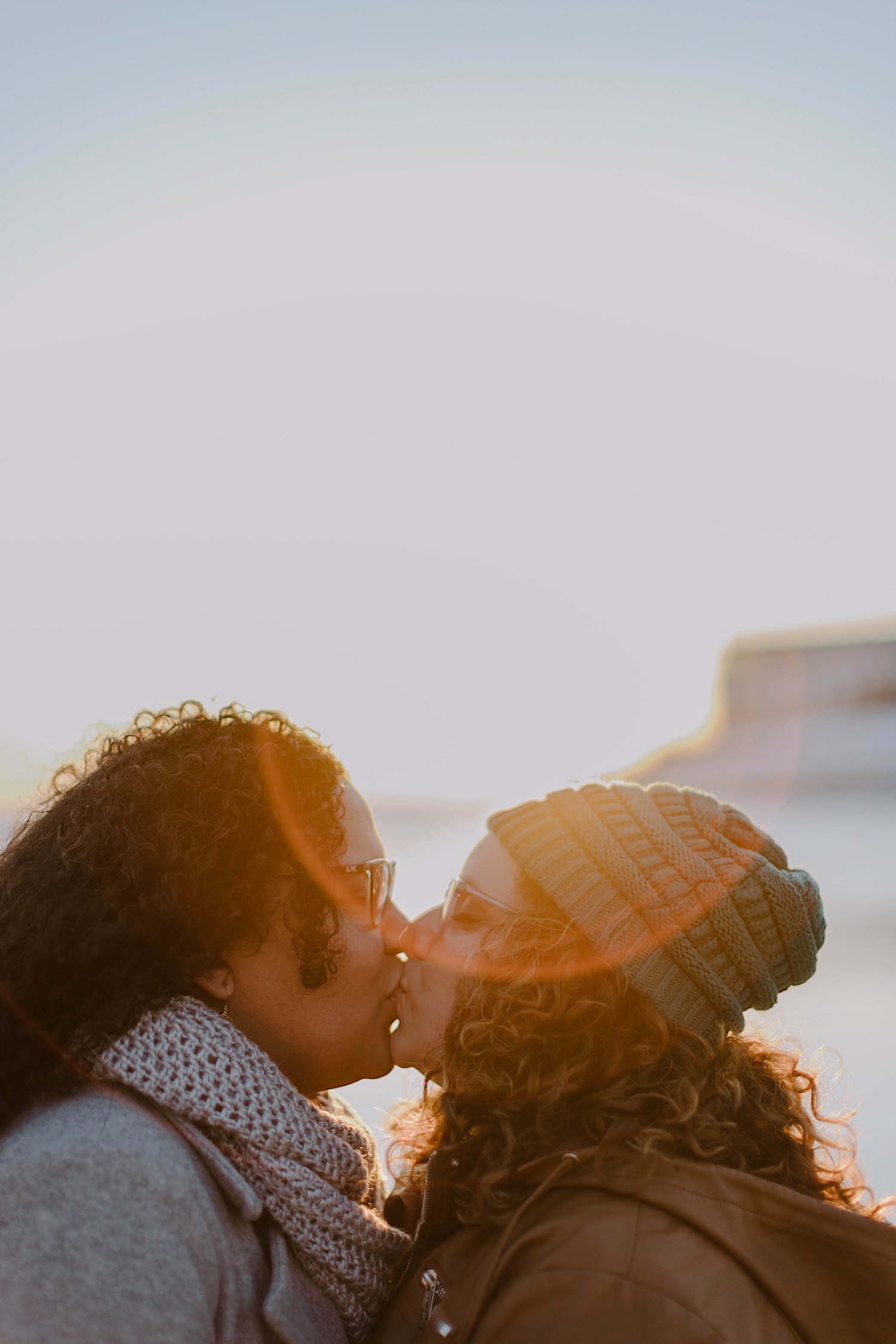 Couple kiss in the sunlight at sunrise wearing winter clothes