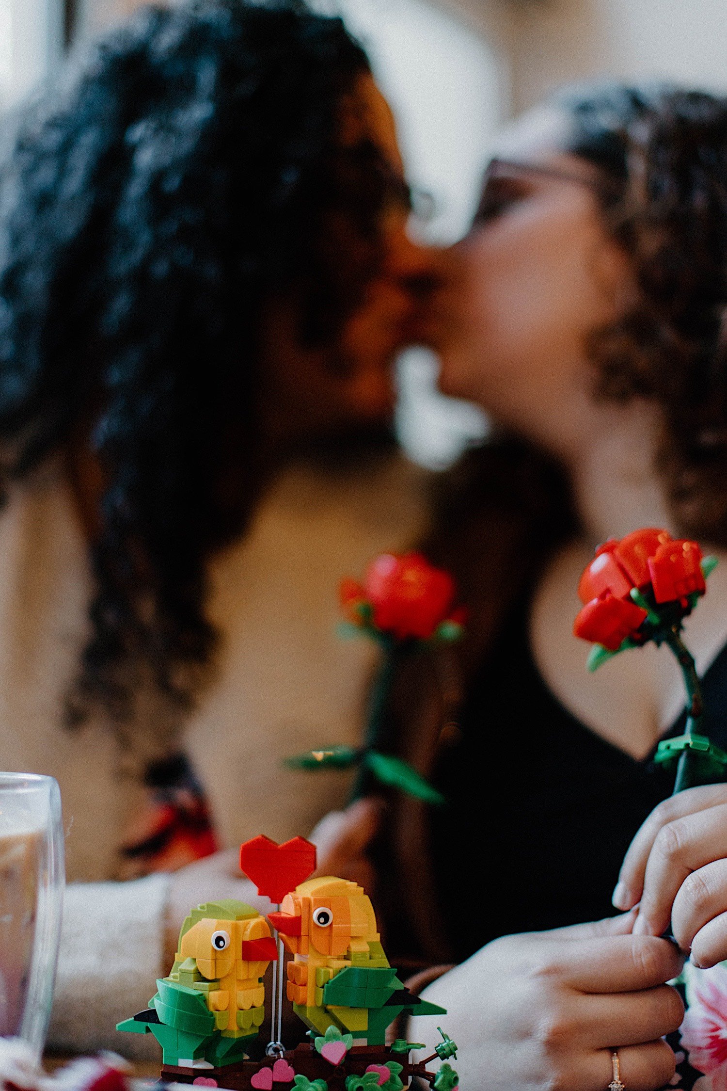 Couple kiss while holding Lego roses as Lego parrots kiss in front of them