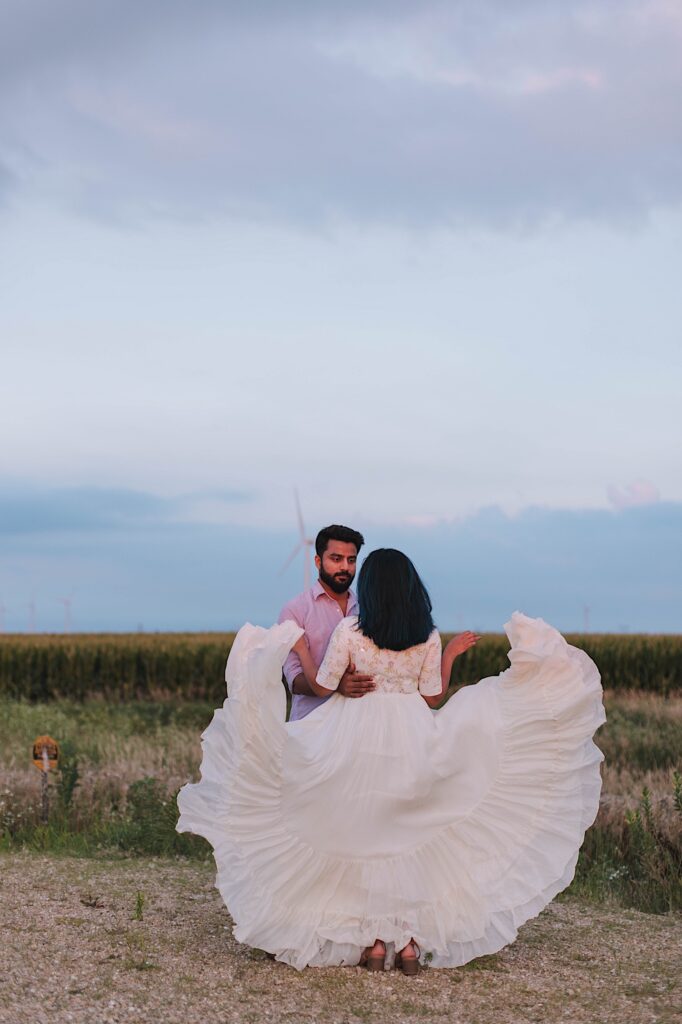 A couple dance with one another with a cornfield behind them.