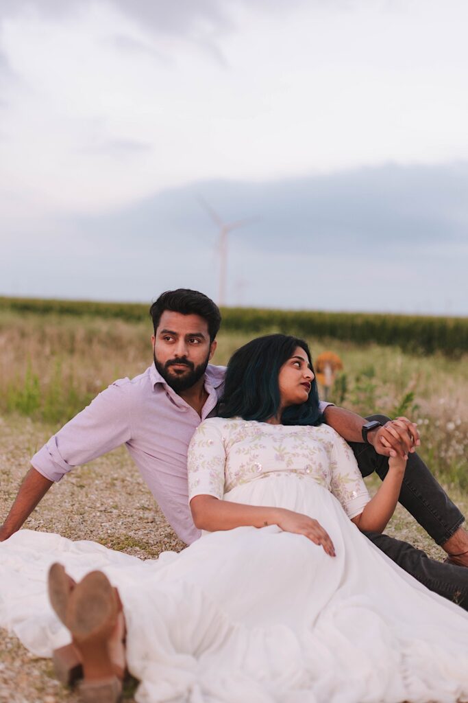 A couple sits in a cornfield and looks in opposite directions while holding hands