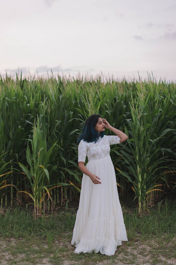 Portrait of a woman in a dress adjusting her hair while standing in front of a cornfield