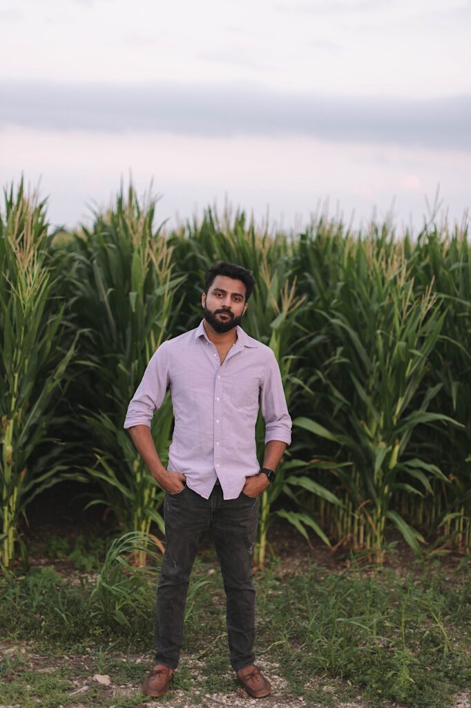 Portrait of a man with his hands in his pockets looking at the camera while standing in front of a cornfield