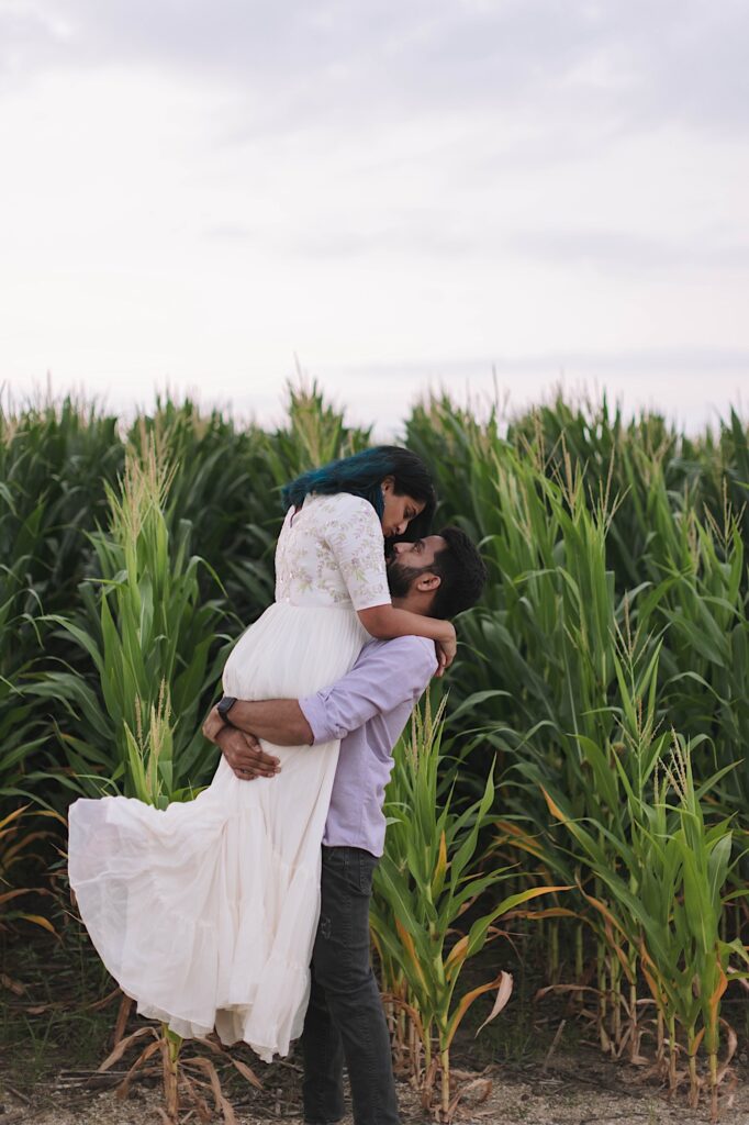 A man lifts his wife into the air as they smile at one another during their newlywed session in a Chicagoland cornfield