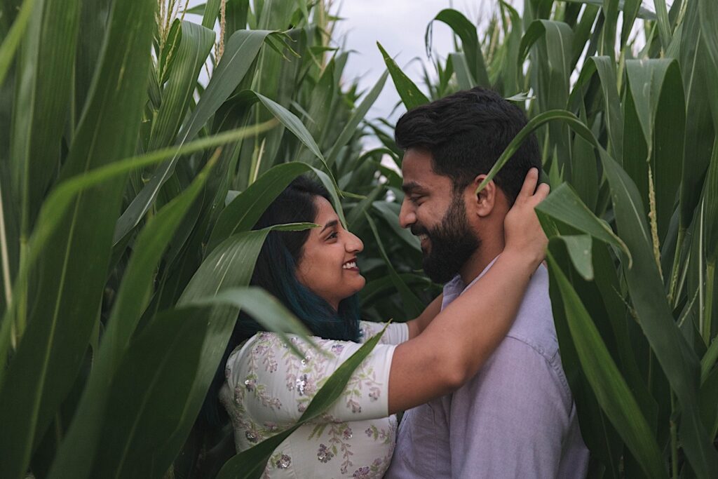 A couple embrace and smile at one another while surrounded by corn during their newlywed session in a Chicagoland cornfield.