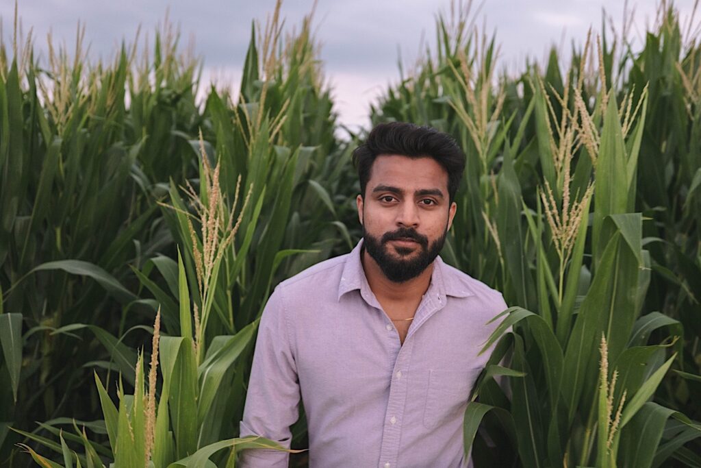 Portrait of a man looking at and walking towards the camera in the middle of a cornfield.