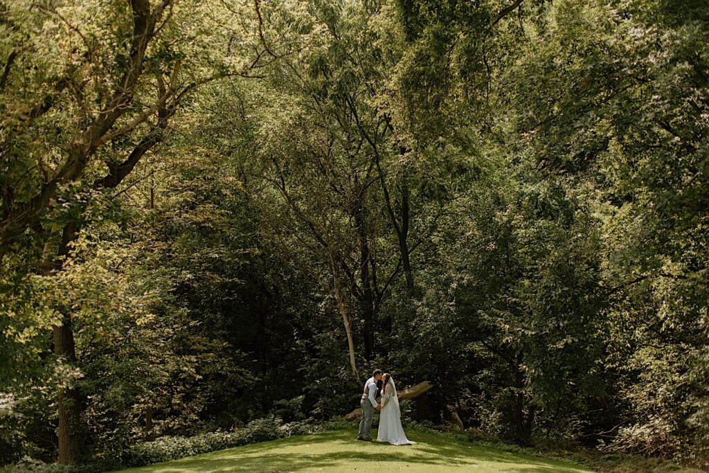A couple in wedding attire kiss in front of a forest