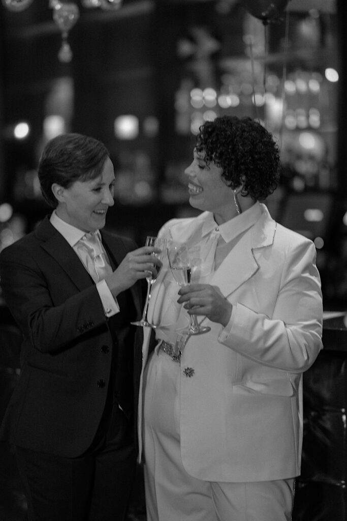 Black and white photo of a couple smiling and toasting their champagne glasses together during their elopement