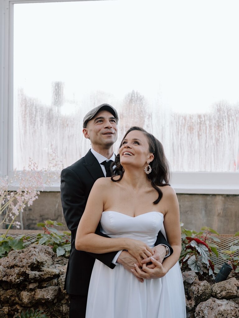 A couple embrace, look at the flowers above them, and smile during their elopement